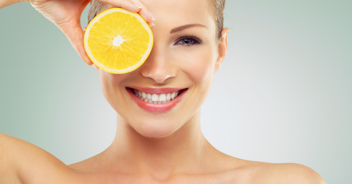 A woman smiling and holding an orange, to show the benefits of Vitamin C